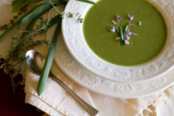 Broccoli and Pea soup in a white bowl next to fresh herbs and a spoon.