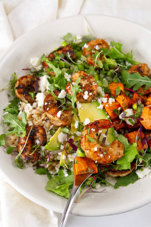 A shrimp bowl with arugula and a fork in the bowl.