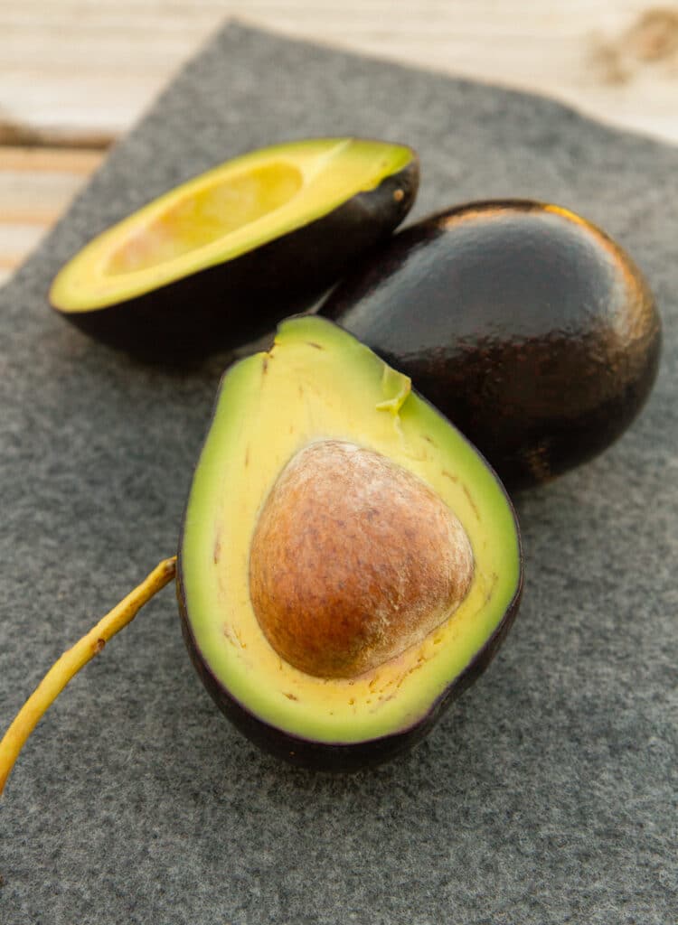 a Mexicola avocado that's been cup open, next to a whole one.