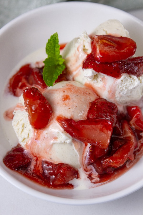 strawberries on top of vanilla ice cream with a sprig of mint.