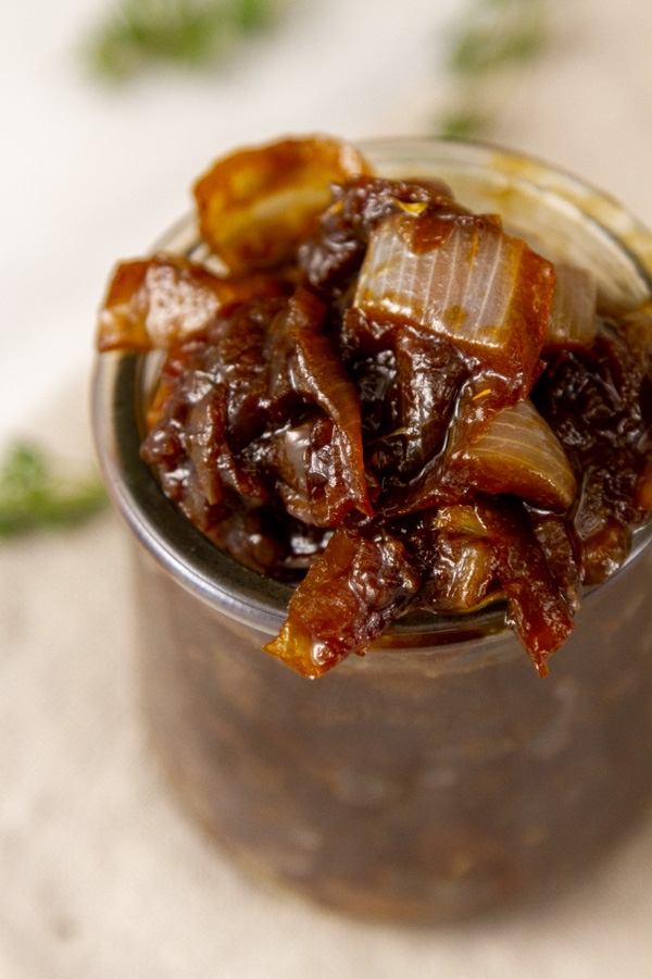 looking down into a glass jar filled with cooked onions, fresh thym ein the background.