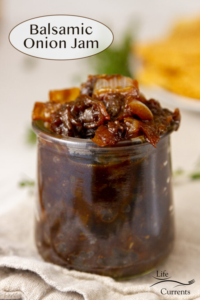a glass jar filled with Balsamic Onion Jam in front of a plate of crackers and some fresh thyme