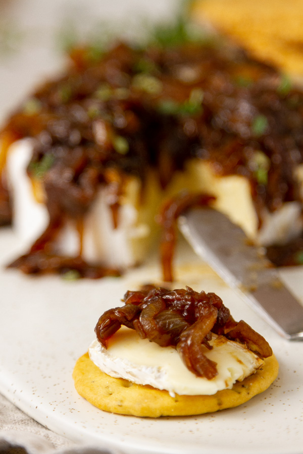 onion jam served on brie and spread on a cracker in front of the round of brie with a knife