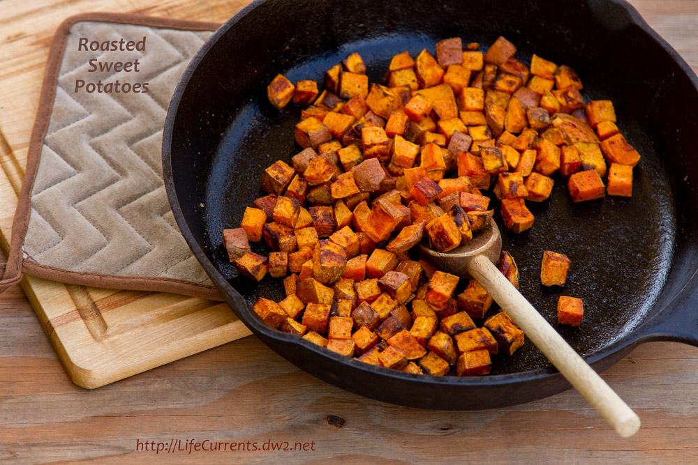 cubes of sweet potatoes in a cast iron skillet with a wooden spoon