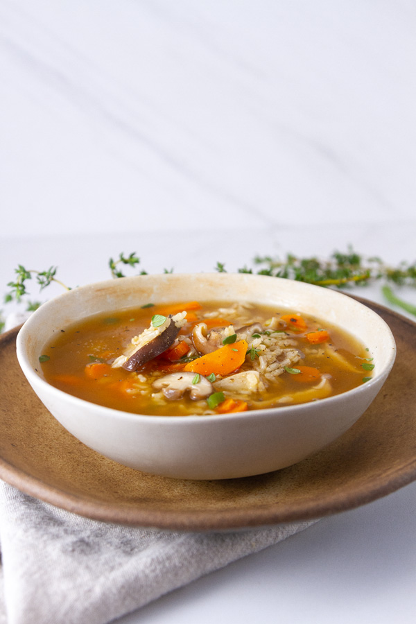 a bowl of soup on a brown plate with fresh herbs in the background