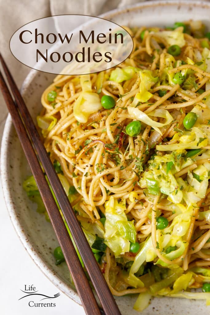 Chow Mein Noodles with cabbage and green peas in a bowl with wooden chopsticks on the left.
