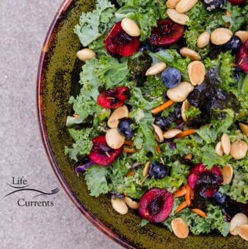 a square crop of a big bowl of kale salad topped with fruits and vegetables.