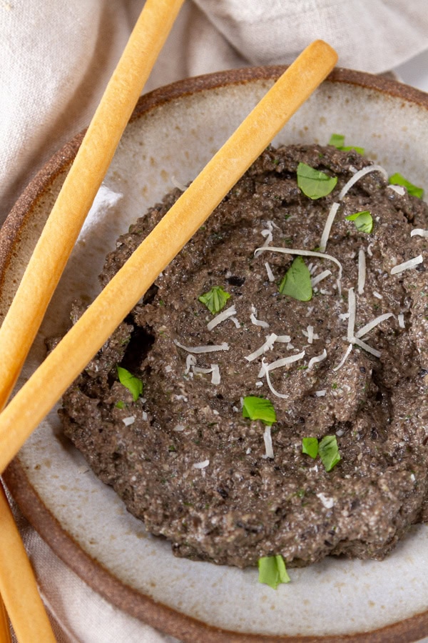 black olive spread in a bowl with breadsticks on the side.
