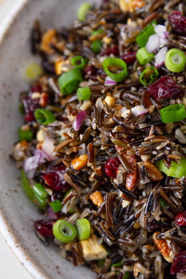 close up on salad filled with rice, veggies, fruits, and nuts.