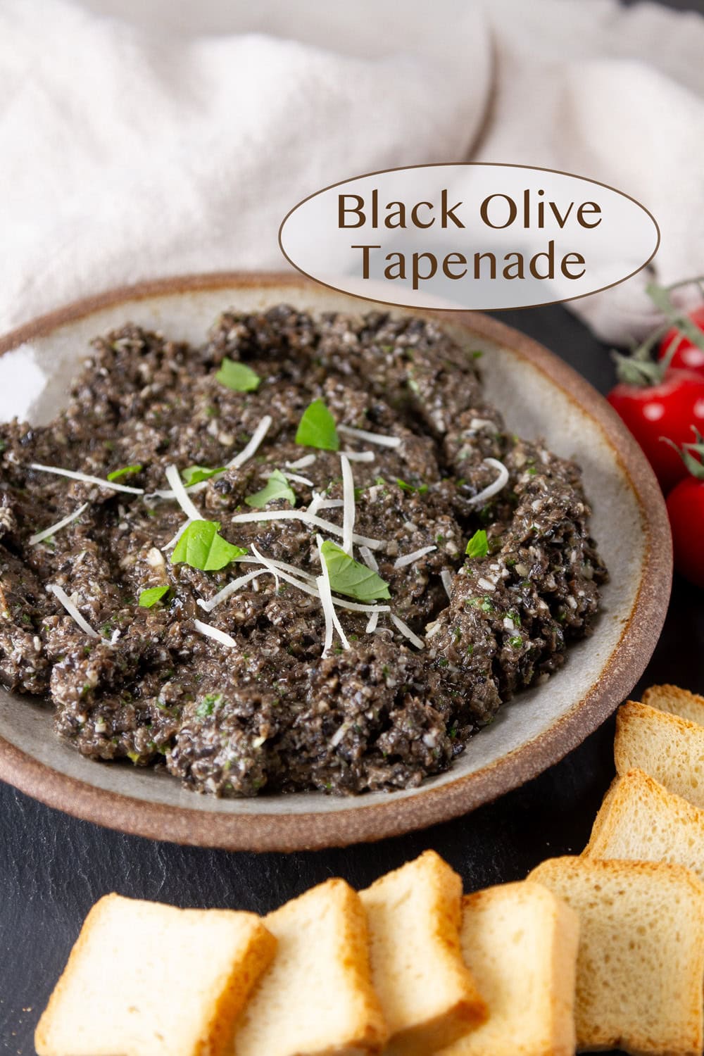 a small serving bowl filled with black olive tapenade and crackers around the bowl.