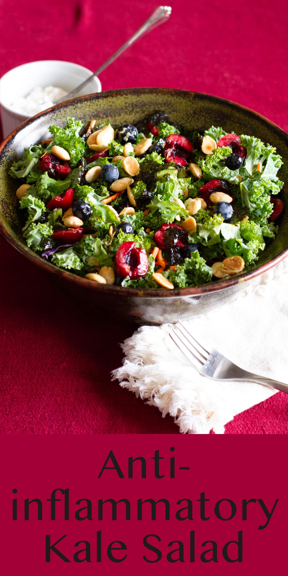 a big bowl of Anti-inflammatory Kale Salad on a red table cloth a small bowl of cottage cheese with a spoon it in the upper left and a white napkin in the lower right.