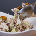 forks picking up some chicken salad out of a white bowl.