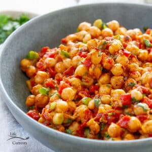 square crop of a blue bowl filled with nacho roasted chickpeas with cilantro and green onions on top.