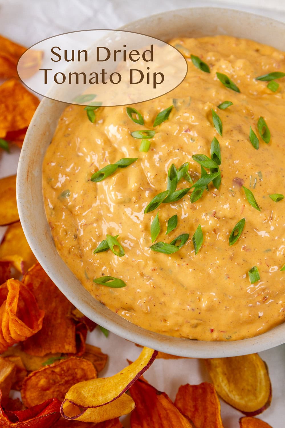 A bowl of sun dried tomato dip surrounded by vegetable chips.