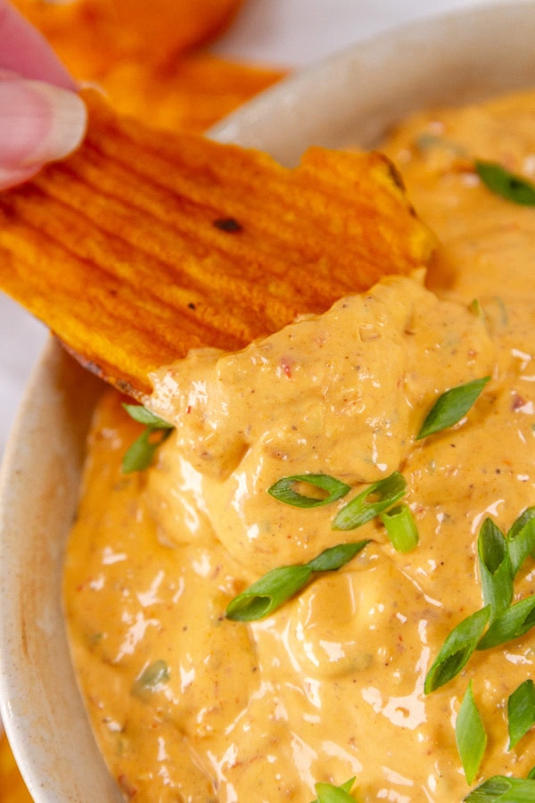 a chip being dipped into dip garnished with green onions.