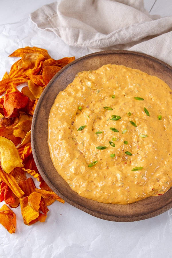 A brown bowl filled with sun dried tomato dip and some chips and a cloth napkin next to the bowl.