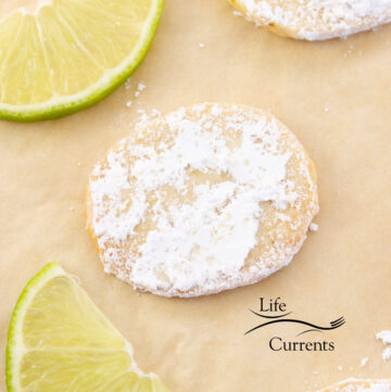 a cookie coated in powdered sugar with slices of lime around it.