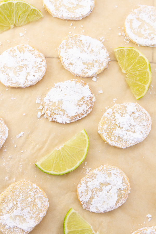 many cookies on a piece of parchment paper with slices of lime.
