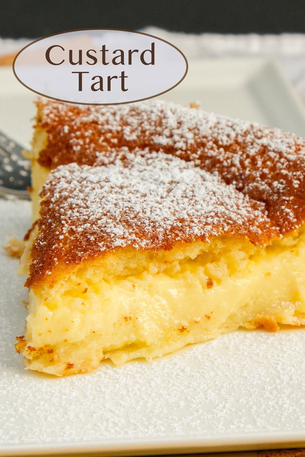 a slice of custard tart on a white plate with powdered sugar on top.