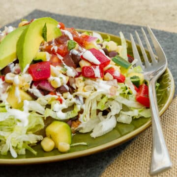square crop of a tostada with corn salad on a green plate with a fork.