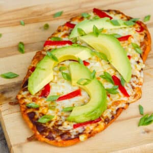square crop of a flatbread pizza on a wooden cutting board.