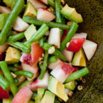 looking down into a summer salad filled with green beans, peaches, corn, and avocado.