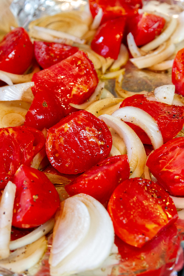 tomatoes and onions sliced and ready to roast on a baking sheet.