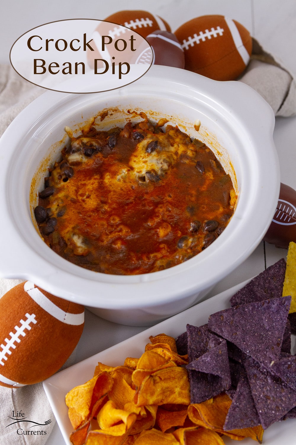 a small white crock pot bowl filled with bean dip, surrounded by chips and footballs.