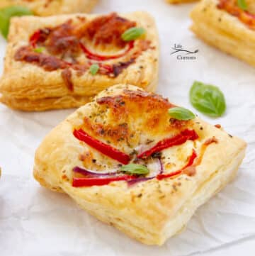 square crop of some puff pastry pizza tarts on parchment paper with fresh basil leaves around.