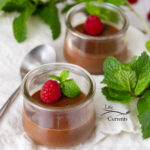 square crop of two glass jars of chocolate dessert topped with raspberries and fresh mint.