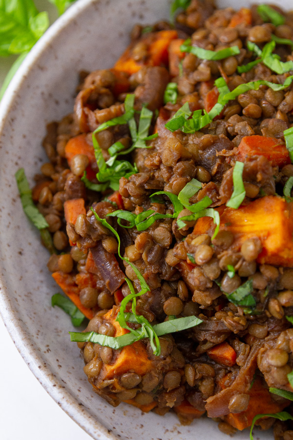close up on cooked lentils and vegeatble in a white bowl garnished with chopped basil.