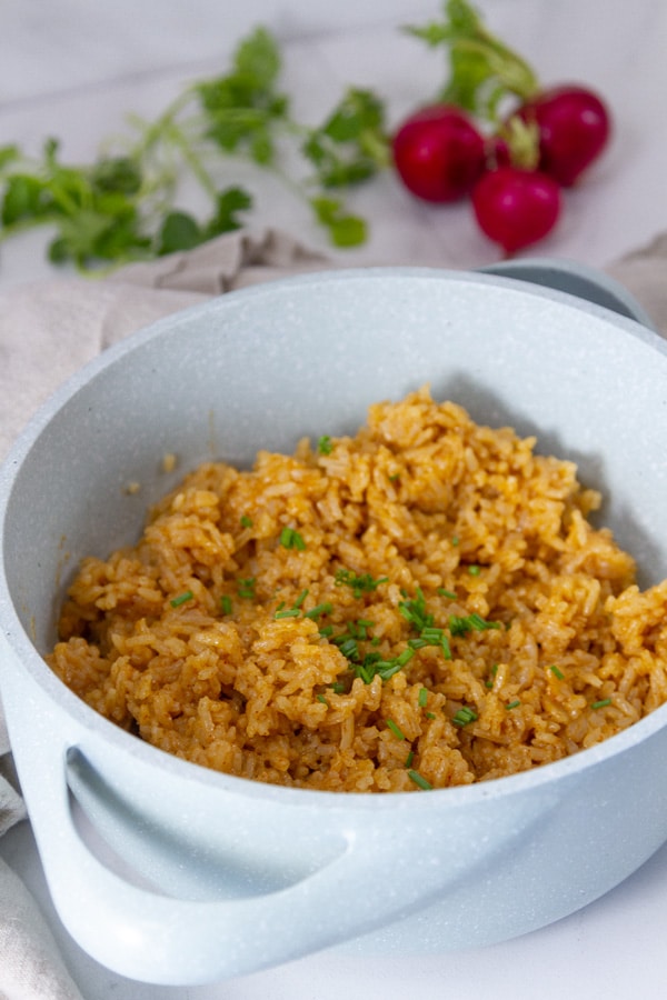 cooked rice in a small blue pot with handles in front of some cilantro and radishes.