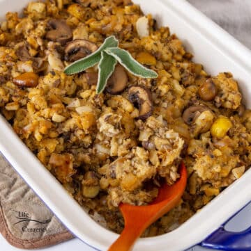 stuffing in a casserole dish with a wooden spoon, topped with 3 sage leaves.