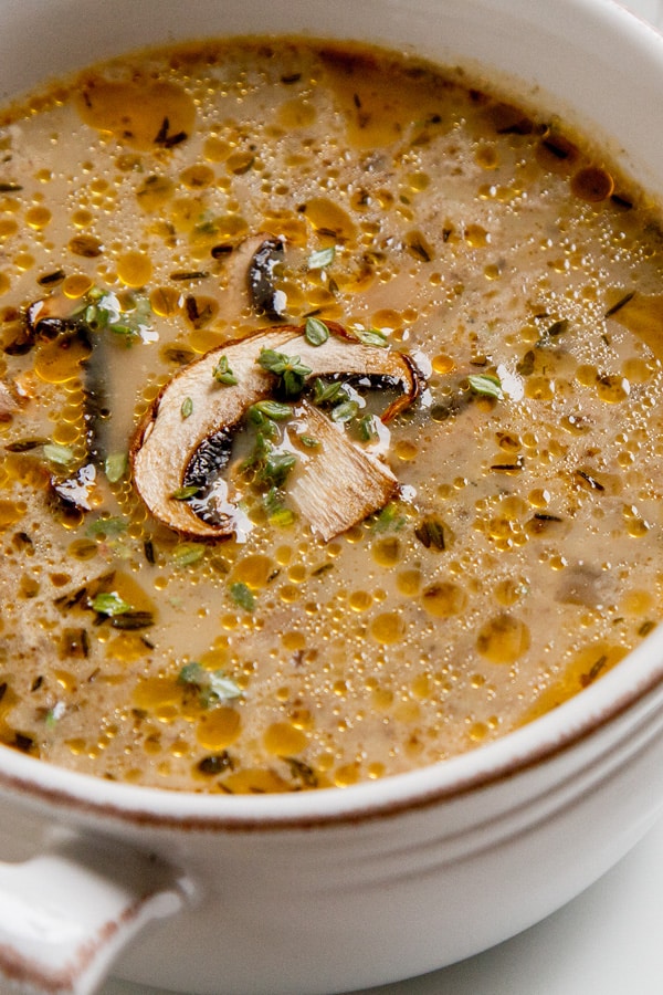 close up on a bowl of mushroom soup with sauteed mushrooms garnished on top of the soup.