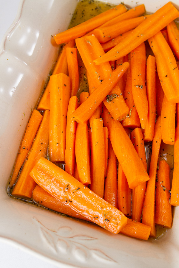 raw cut carrots in a dish with maple and herb glaze on them