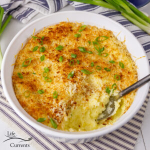 square crop of mashed potato casserole in a white dish with a serving spoon in it.