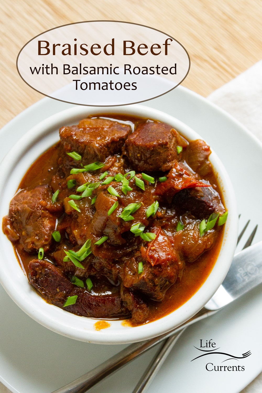 a white bowl filled with braised beef topped with green onions and a fork and knife next to it.