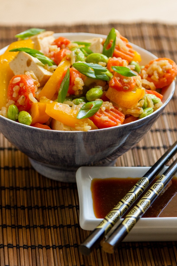 a ceramic bowl filled with veggies and tofu with a small white dish with teriyaki sauce and chopsticks on it.