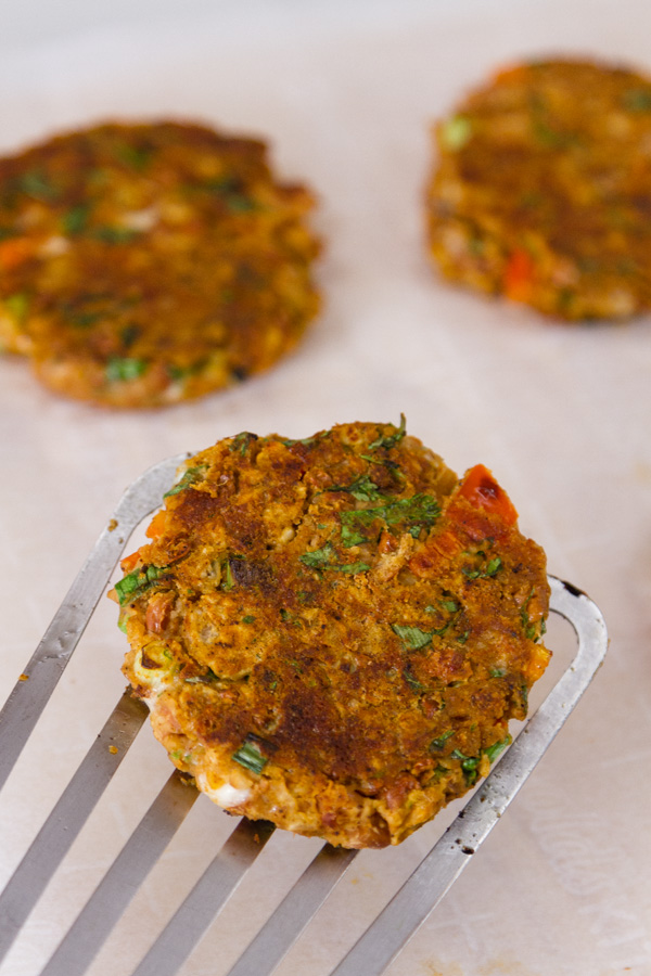 Falafel patties, cooked and one is being picked up on a spatula