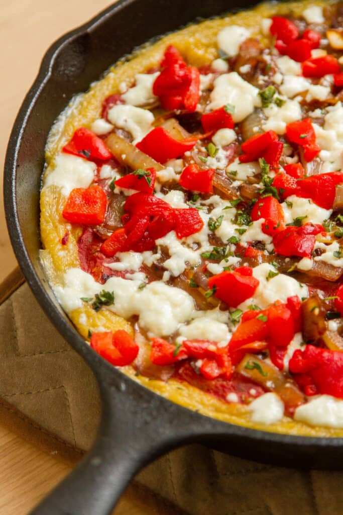 a cast iron skillet filled with a polenta pizza topped with lots of veggies.