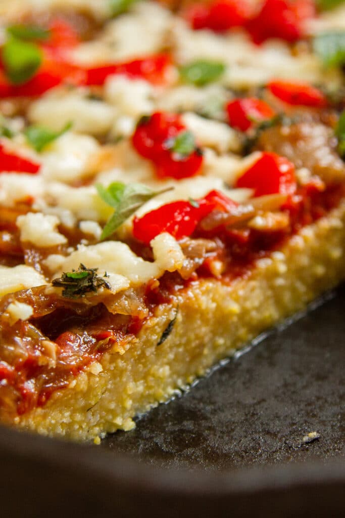 close up on the polenta crust of the polenta pizza in a cast iron skillet.