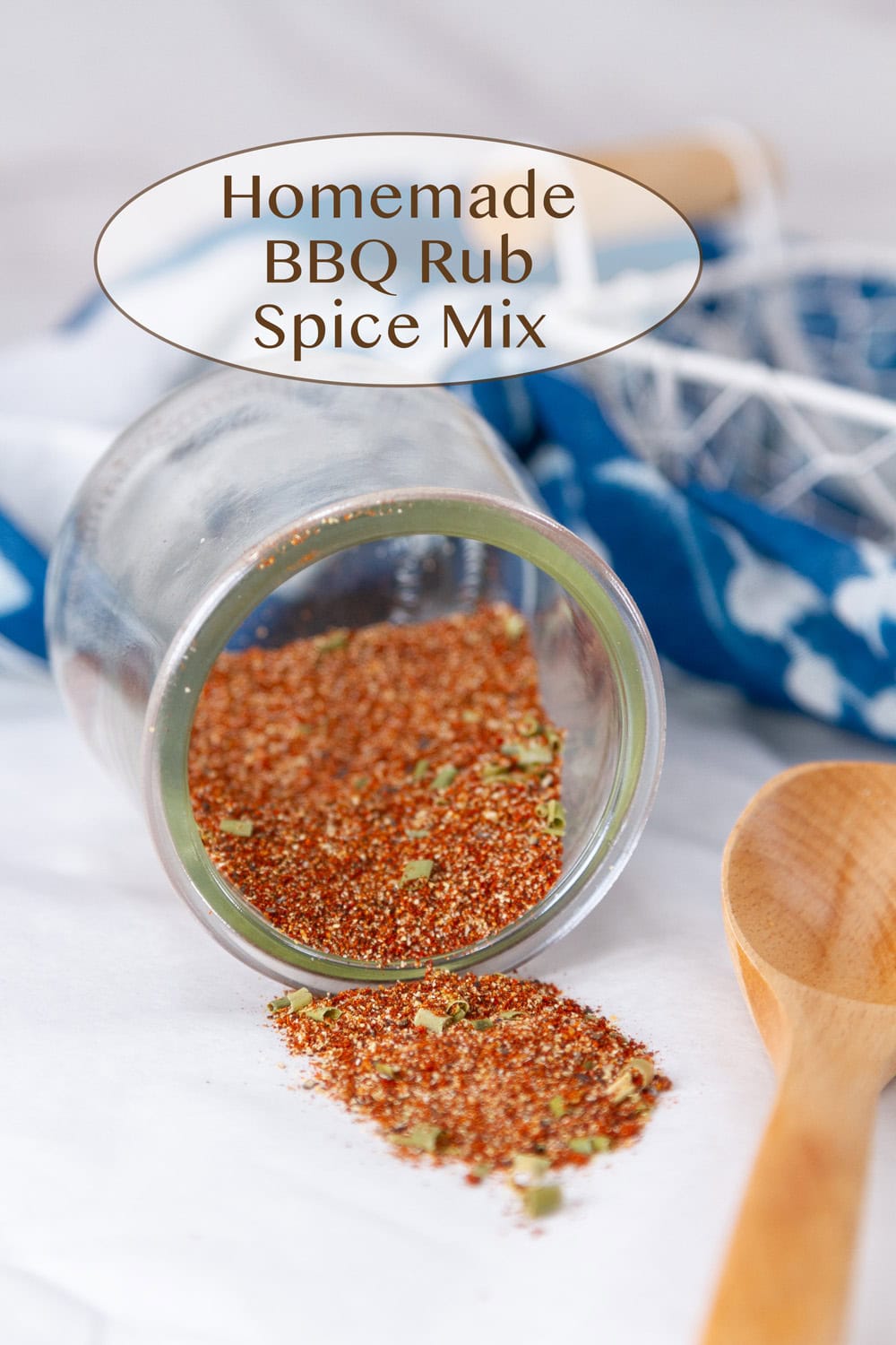 spice mix in a glass jar that's tipped over so the spice spilled out with a wooden spoon and a blue cloth.
