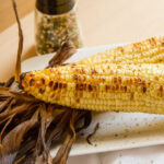 two ears of corn that have been grilled in front of a bottle of spice mix.
