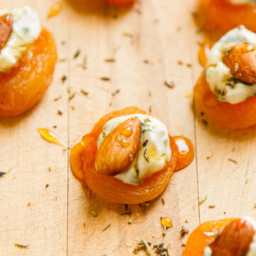 dried apricots stacked with cheese spread, almonds, and honey drizzle on a wooden cutting board.