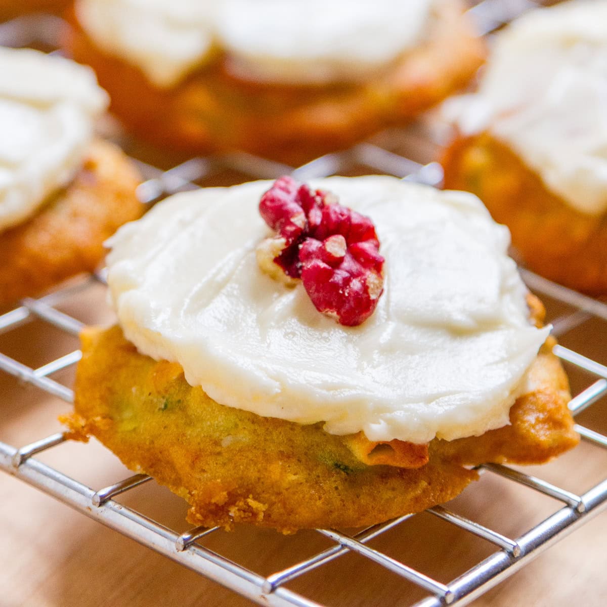 a frosted cookie on a wire rack with a red walnut on top.