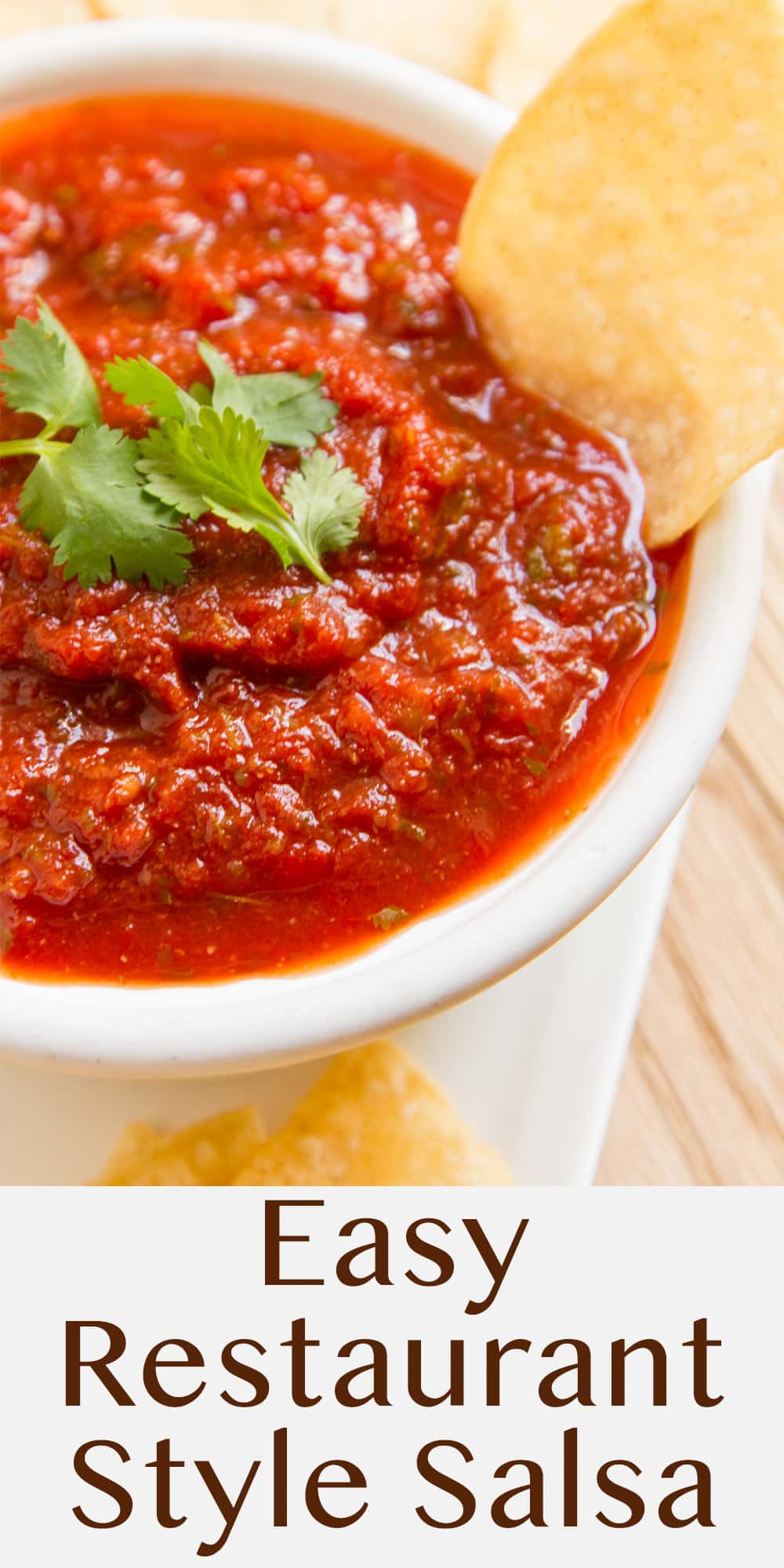 a bowl of salsa with a tortilla chip in it and a cilantro leaf on top.