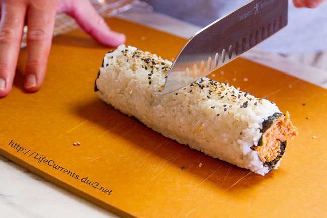 cutting an inside out tuna roll with a knife.