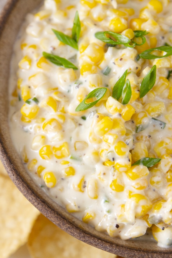 close up on creamy corn in a bowl topped with green onions.