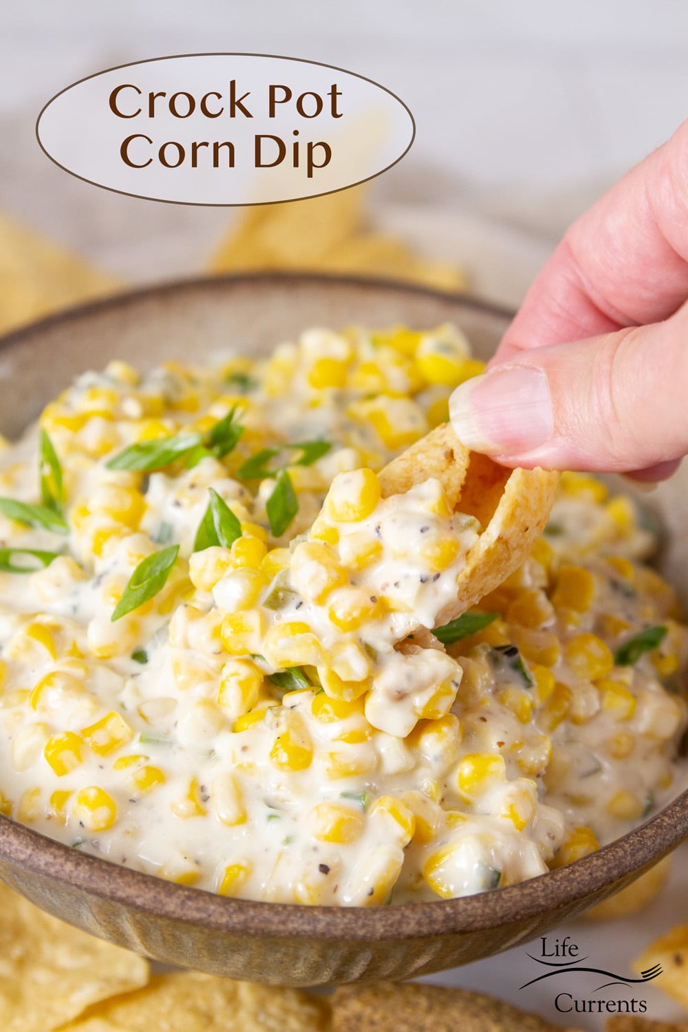 a hand dipping a chip into a bowl of crock pot corn dip.