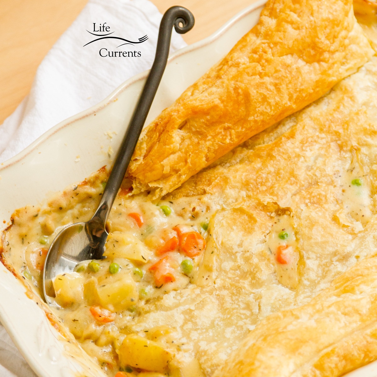 looking into the dish of creamy pot pie filling topped with puff pastry and there's a serving spoon.